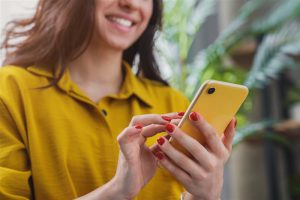 Woman in yellow shirt holding a yellow phone smiling 