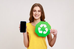 Happy teenager girl in yellow T-shirt holding phone with blank screen and recycle symbol environment Icon, looking smiling at camera.